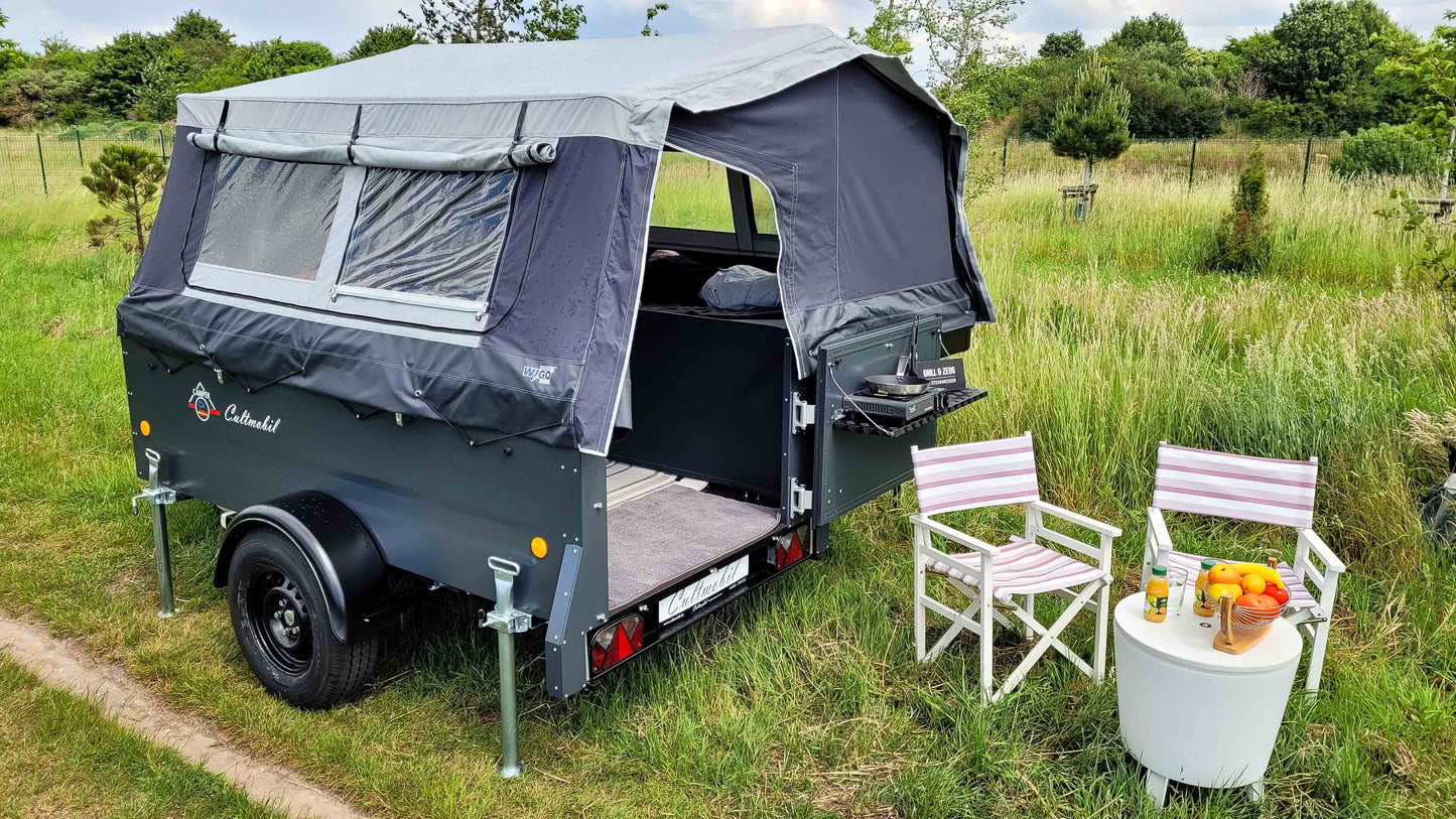Campinganhänger mit nassem Zelt auf einer Wiese. 