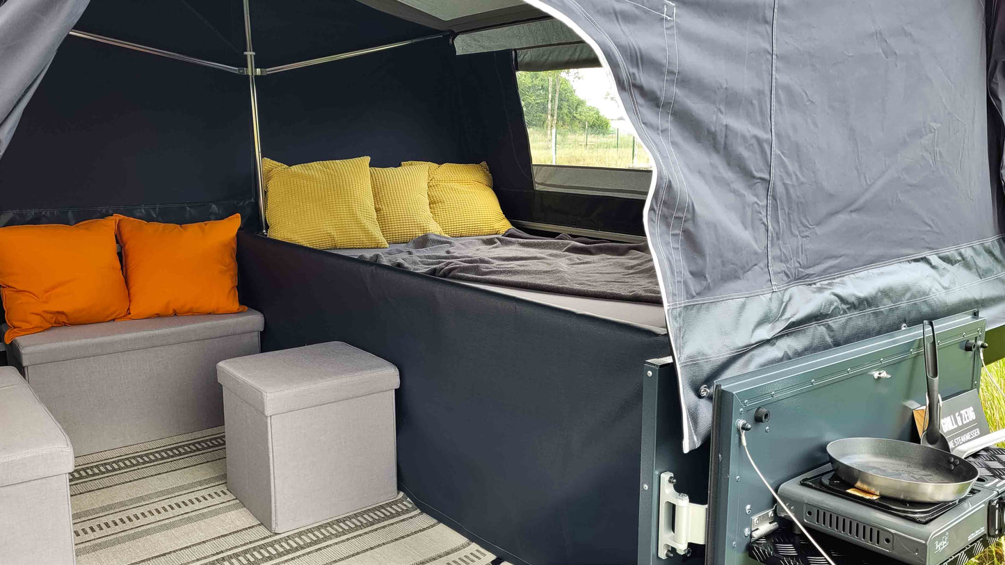 Innenansicht eines Klappcamper auf die Sitzgelegenheiten und Kissen sowie Decke und Teppich