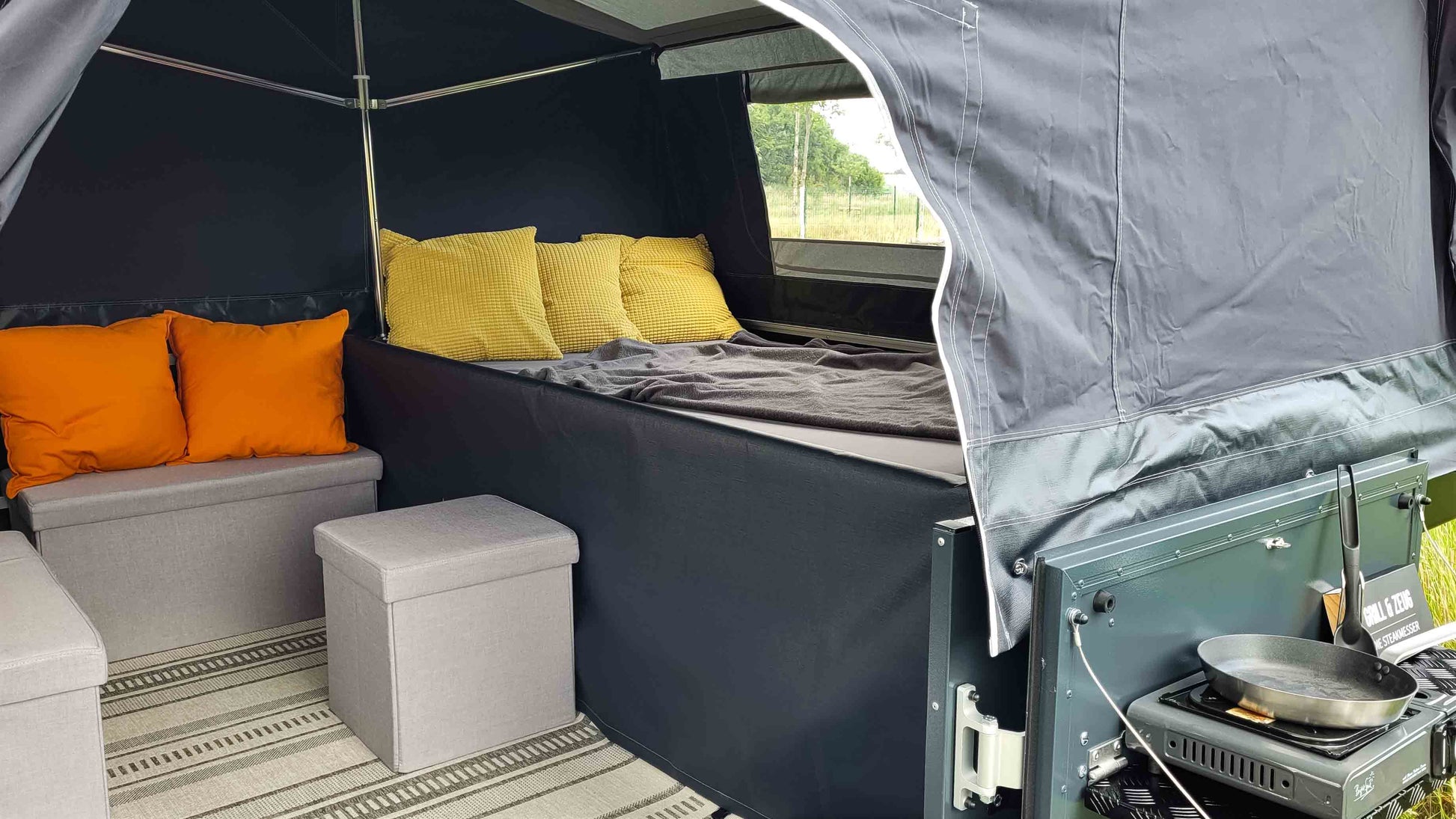 Innenansicht eines Klappcamper auf die Sitzgelegenheiten und Kissen sowie Decke und Teppich