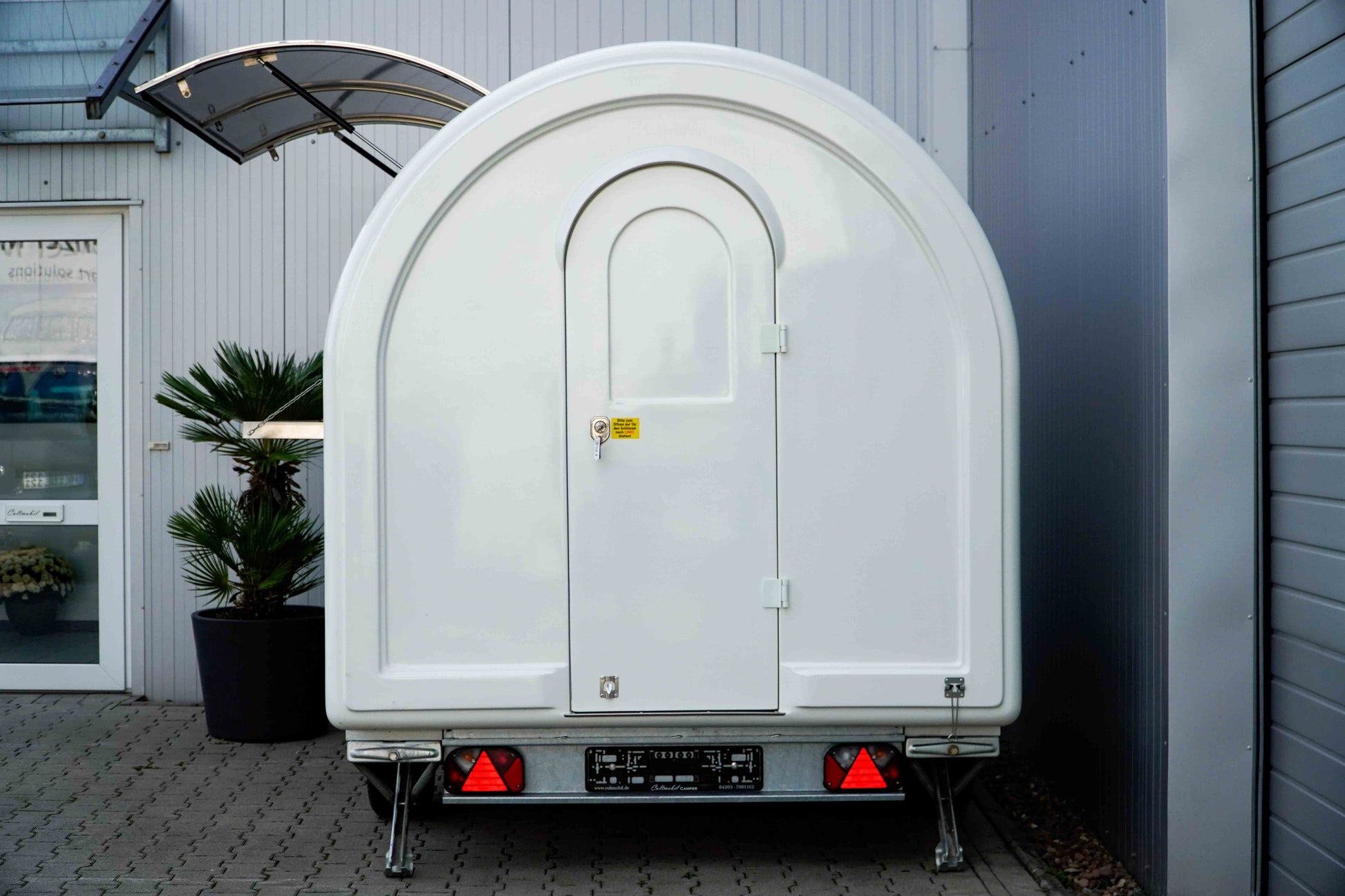 Ein weißer Verkaufsanhänger von der Seite mit Blick auf die Eingangstür 
