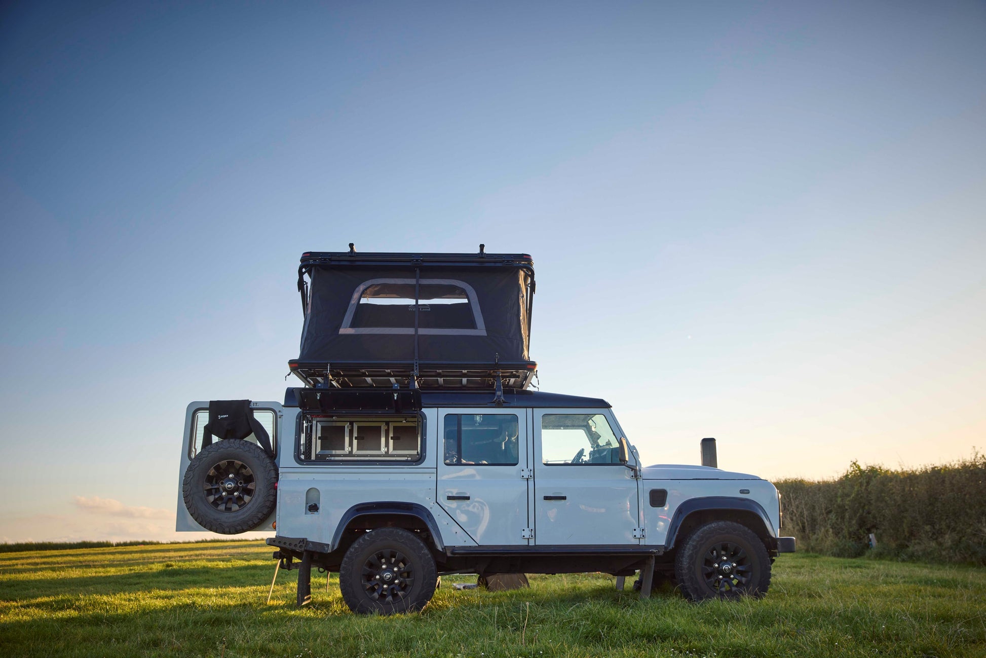 Dachzelt für Auto und Minicamper, 2 Personen, Hartschale mit Z-förmigem Bügel, auf einem Offroad-Wagen montiert, stehend auf einer Wiese