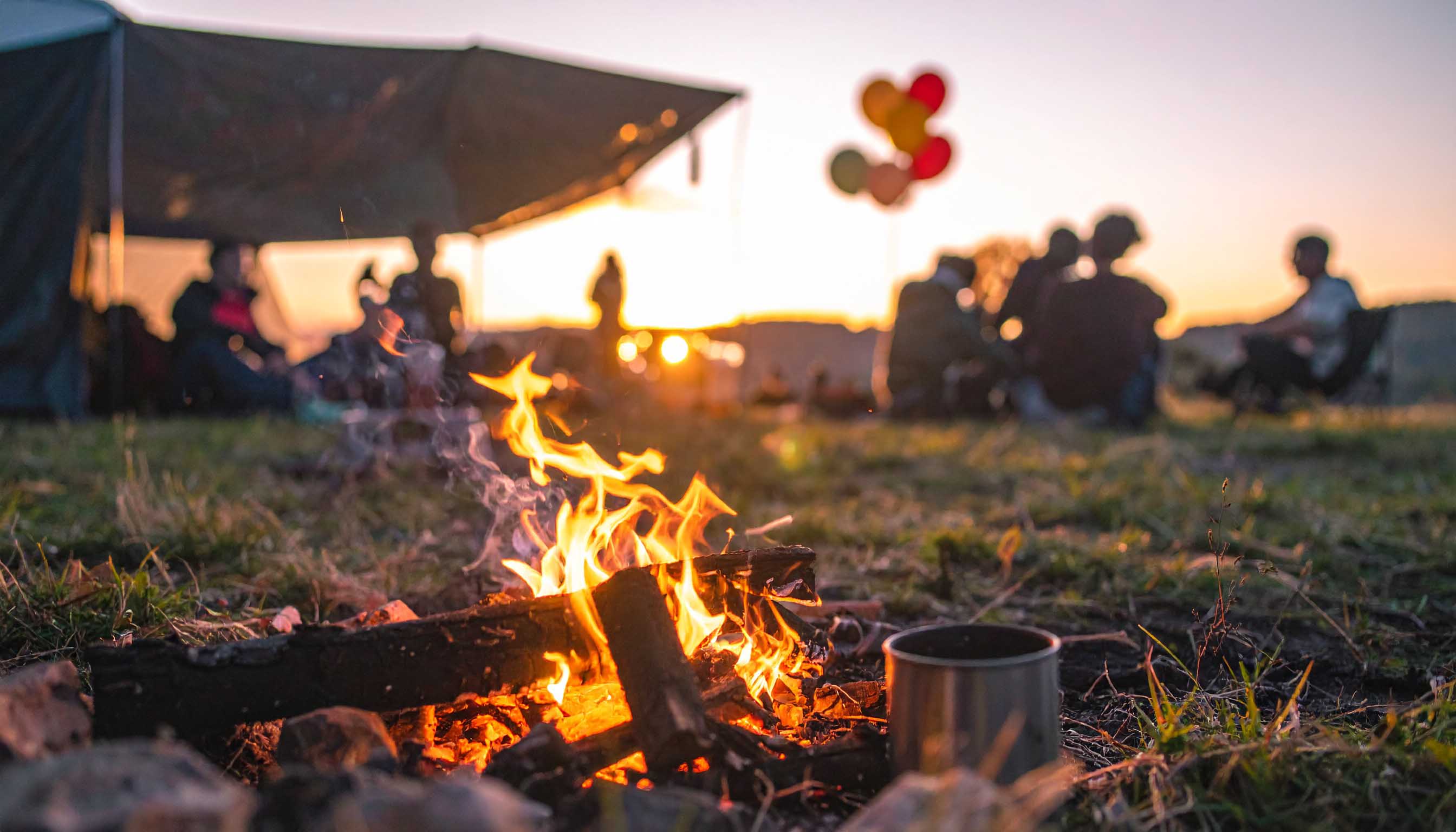 Ein Bild von Menschen die gemütlich an einer Feuerstelle neben einem Zelt zusammensitzen