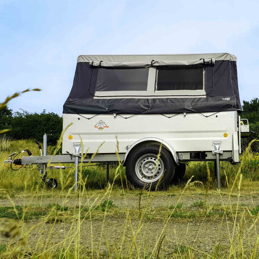 Seitenansicht eines Faltcaravans mit aufgebautem Zelt und Stützen auf einer Wiese