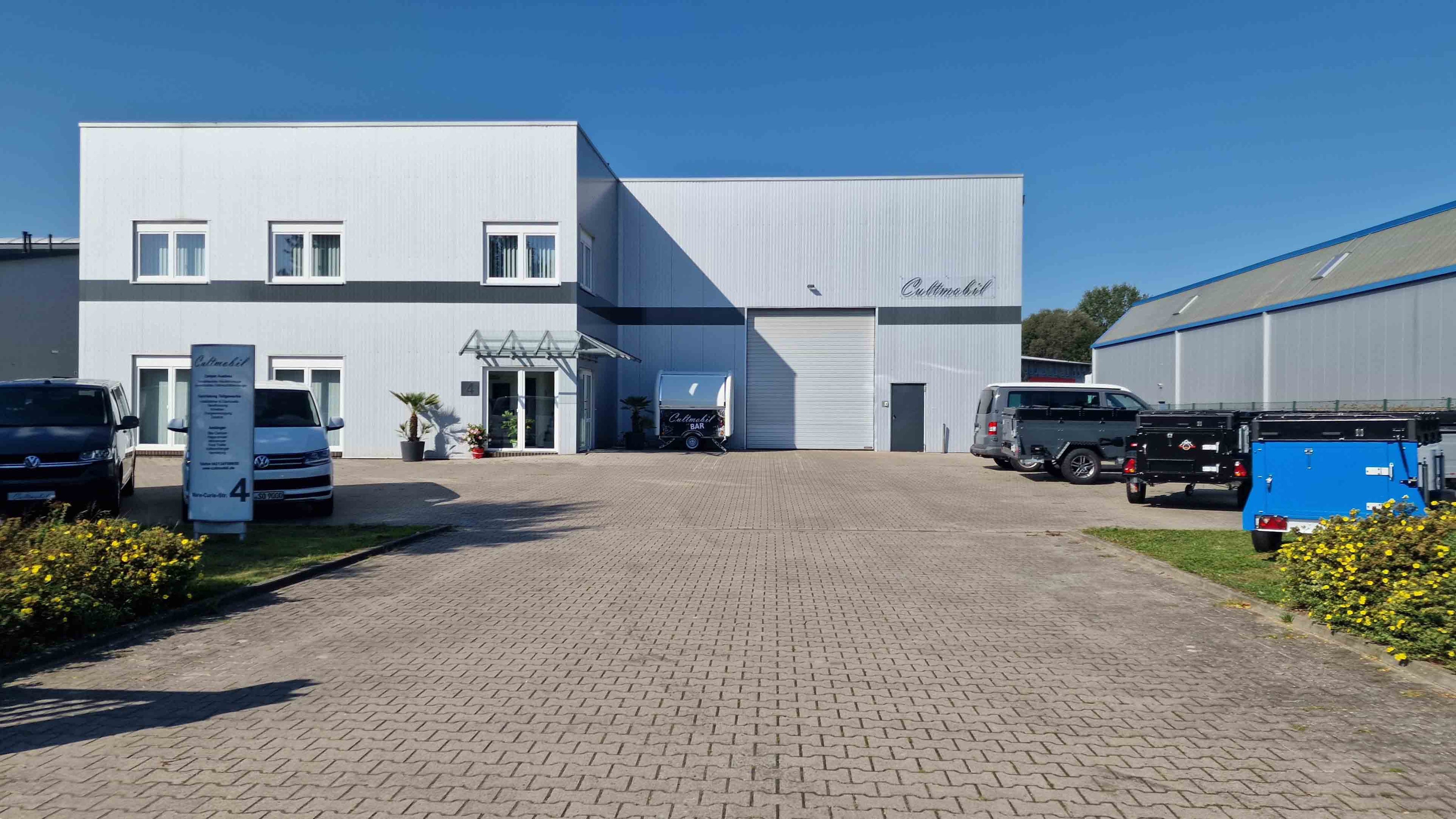 Eine Gewerbehalle von vorne mit einigen Fahrzeugen auf dem Parkplatz